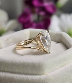 a gold ring with a pear shaped diamond in it sitting on a white velvet box