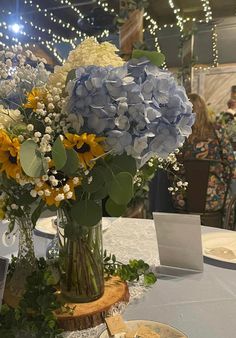 a vase filled with blue and yellow flowers on top of a white table cloth covered table