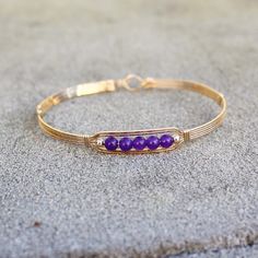 A sweet little bracelet of five strands of 14kt gold filled wire with a center design featuring five 4mm genuine amethyst beads and accented with two smaller beads. Perfect for that February birthday girl! Stackable, too, along with many of my other wirewrapped bracelets! The sturdy built-in hook and eye clasp is easy to get on and off by yourself. Choose the size you need for a comfortable custom fit. Also available in sterling silver. Adjustable Hand-strung Cuff Bracelet Gift, Gold Hand-strung Wrap Bracelet Gift, Gold Hand-wrapped Bracelets For Gifts, Hand Wrapped Gold Bracelets As Gift, Hand Wrapped Gold Bracelets For Gift, Friendship Hand Wrapped Bangle Bracelet, Dainty Adjustable Wire Wrapped Beaded Bracelets, Adjustable Dainty Gold Bangle Bracelet, Adjustable Hand-strung 14k Gold Filled Bracelet