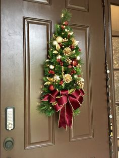 a christmas tree hanging on the front door with red bows and ornaments around it's base