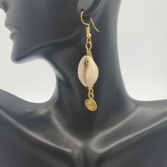 A must have pair of earrings. Dainty, but has that must needed elegant touch to it! FUN FACTS: In Africa, and in the Americas, the cowrie symbolize destiny and prosperity and in many cases hold significant spiritual and even monetary value. The cowrie shell was an universal form of currency whose relevance weaved into the culture of Ancient African societies. The durable and light-weight characteristics of the shells made them an ideal trading currency long before the world adopted pounds, dolla Cowry Shell Earrings, African Femininity, Cowrie Shell Necklace, Cowry Shell, Brass Hoop Earrings, Seashell Jewelry, Brass Hoops, Earrings Dainty, Cowrie Shell