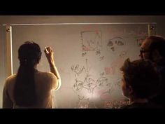 two people standing in front of a whiteboard with writing on it and one person holding a marker