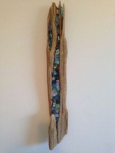 a piece of driftwood hanging on the wall with beads and stones embedded in it