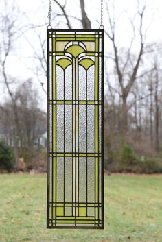 a stained glass window hanging from a chain in front of a grassy area with trees