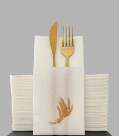 a stack of white paper napkins with gold forks and spoons sitting on top of each other