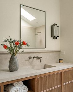 a vase with flowers in it sitting on a bathroom counter next to a sink and mirror