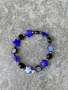 A black, bronze, and blue bracelet. beads are glass. 2 inches in length. 3 inches in width Adjustable Blue Bracelets With Black Beads, Black Jewelry With Colorful Czech Glass Beads, Blue Bracelet With Black Beads Jewelry, Blue Bracelet With Black Beads, Adjustable Black Czech Glass Jewelry, Adjustable Blue Beaded Bracelets With Black Beads, Adjustable Blue Czech Glass Stretch Bracelet, Blue Jewelry With Round Black Beads, Blue Hematite Jewelry For Gift