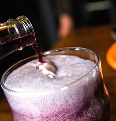 someone is pouring red wine into a purple drink in a glass on a wooden table