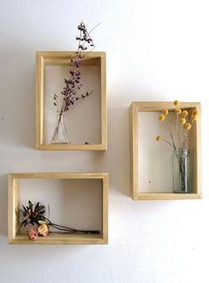 three square wooden shelves with vases and dried flowers in them on the white wall