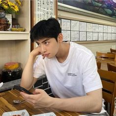 a young man sitting at a table looking at his cell phone while he eats food