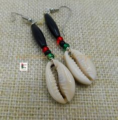 two white shells with black and red beads are hanging from silver earwires on a beige cloth