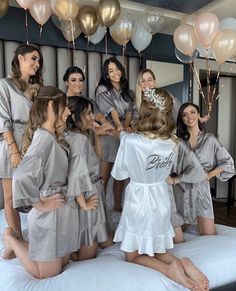 a group of women standing around each other on a bed with balloons in the background