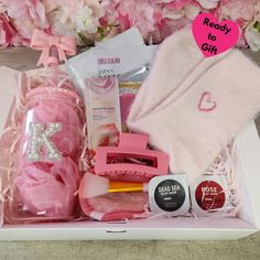 a pink gift box with personal care items in it and some flowers behind the box