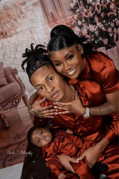 a woman holding a baby in her lap and smiling at the camera while she is wearing an orange dress