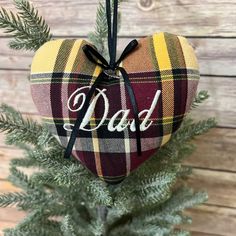 a plaid heart ornament with the word dad on it hanging from a tree