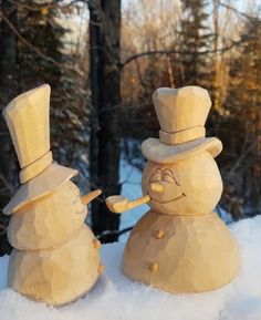 two snowmen made out of wood standing in the snow with trees in the background