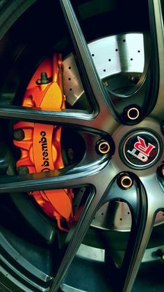 an orange brake pad sits on the front wheel of a car with black spokes