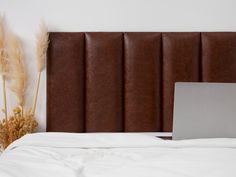 an open laptop computer sitting on top of a bed next to dried plants and a white wall