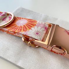 an orange and pink flowered belt on a white cloth with gold buckles,