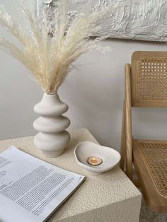 a white vase sitting on top of a table next to a book and a candle