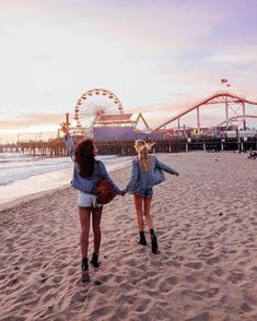 two girls walking on the beach with their arms in the air and ferris wheel in the background