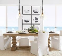 a dining room table with white chairs and pictures on the wall in front of it