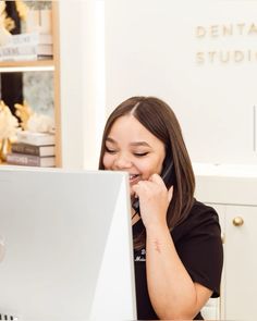 a woman sitting in front of a laptop computer talking on a cell phone and laughing