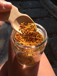 a person holding a wooden spoon over a jar filled with yellow and brown food items