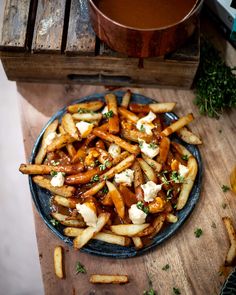 french fries with cheese and herbs on a blue plate next to a pot of soup