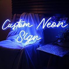 a neon sign sitting on top of a bed next to a night stand with flowers