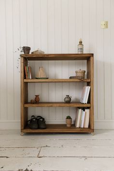 a wooden shelf with books and other items on it, against a white painted wall