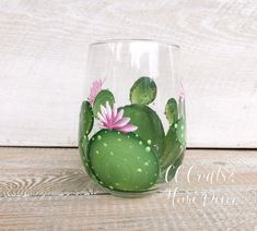 a green glass with pink flowers painted on the outside and inside, sitting on a wooden surface