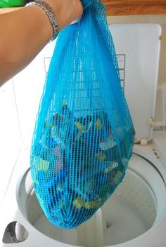 a person holding a blue mesh bag over a washing machine with the words washing logos or any toy for that matter?