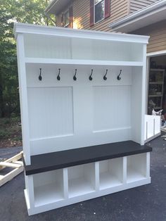 a white and black bench in front of a house with hooks on the back wall