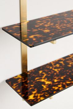 two glass shelves with gold and black designs on the bottom one shelf has a metal bar at the top