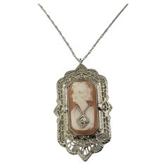 Vintage 12 Karat White Gold and Diamond Reversible Cameo Pendant- This stunning reversible 12K white gold filigree pendant pictures a lovely lady in profile decorated with one round single cut diamond on one side. The reverse side features elegant black onyx accented with one round single cut diamond. Suspends from a classic cable necklace. Approximate total diamond weight: .02 ct. Diamond clarity: VS2 Diamond color: H Size: 34 mm x 20 mm (pendant) 18 inches (necklace) Weight: 3.9 dwt. / 6.1 gr. Antique White Gold Necklace With Intricate Design, Victorian White Gold Medallion Necklace, Elegant Cameo Jewelry For Formal Occasions, Elegant Cameo Necklace For Formal Occasions, Antique White Gold Filigree Necklace, Antique White Gold Necklace With Filigree, White Gold Filigree Necklace In Oval Shape, White Gold Oval Filigree Necklace, Oval White Gold Filigree Necklace