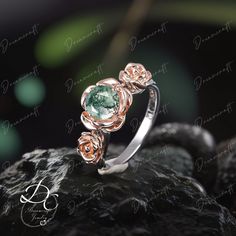 an engagement ring with green and pink stones on top of a black rock in the dark