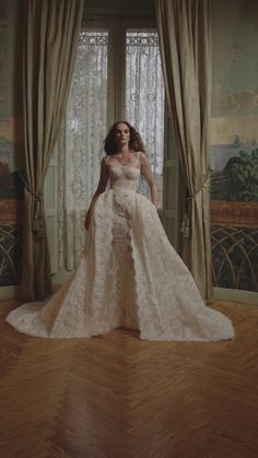 a woman standing in front of a window wearing a wedding dress