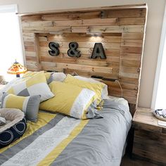 a bed made up with yellow and gray pillows on top of it next to a wooden headboard