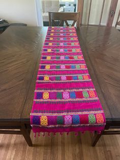 a long table with a pink and green runner on it's end next to a wooden dining room table