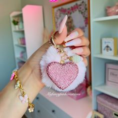 a hand holding a pink heart shaped keychain in front of a white dresser