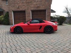 a red sports car parked in front of a brick house with two garage doors open