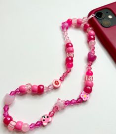 a pink cell phone with a beaded lanyard on it