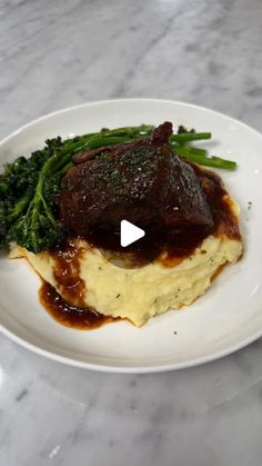 a white plate topped with meat covered in gravy and broccoli on top of a marble counter