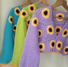 three crocheted sweaters are hanging on a clothes hanger with sunflowers