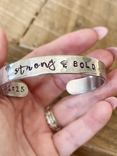 Introducing the Uplift Collection featuring hand stamped metal cuff bracelets with encouraging reminders of who you and whose you and scripture reference. Choose one bracelet: 1. STRONG & BOLD 3/8" CUFF 2. BEAUTIFUL WARRIOR 1/2" CUFF 3. GRACIOUS & KIND 1/4" CUFF 4. MADE WORTHY 1/2" CUFF 5. VICTORIOUS 3/8" CUFF 6. CHOSEN & KNOWN 1/4" CUFF Each bracelet has a scripture reference written on the inside of the cuff. Add a leather wrap bracelet here: https://etsy.me/3koMuWo Add a Rhinestone Bracelet h Beautiful Warrior, Stamp Jewelry, Hand Stamped Cuff Bracelet, Warrior 1, Rhinestone Bra, Hand Stamped Metal, Stamped Spoons, Metal Stamped Jewelry, Metal Cuff Bracelet