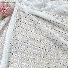 a pink flower sitting on top of a white table cloth next to a piece of fabric