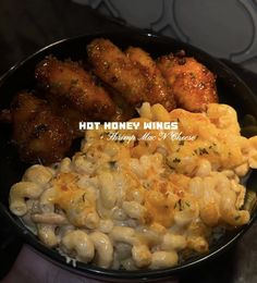 a bowl filled with macaroni and cheese next to chicken wings