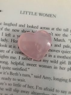 a pink heart shaped stone sitting on top of an open book with the words little women written