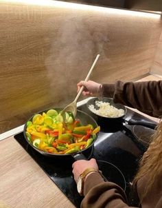 a woman stirs vegetables in a wok on the stove